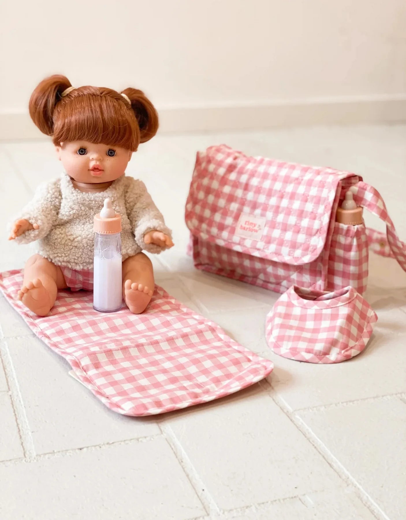 Ensemble pour poupées comprenant sac a couche bavoir et tapis a langer rose a carreaux 